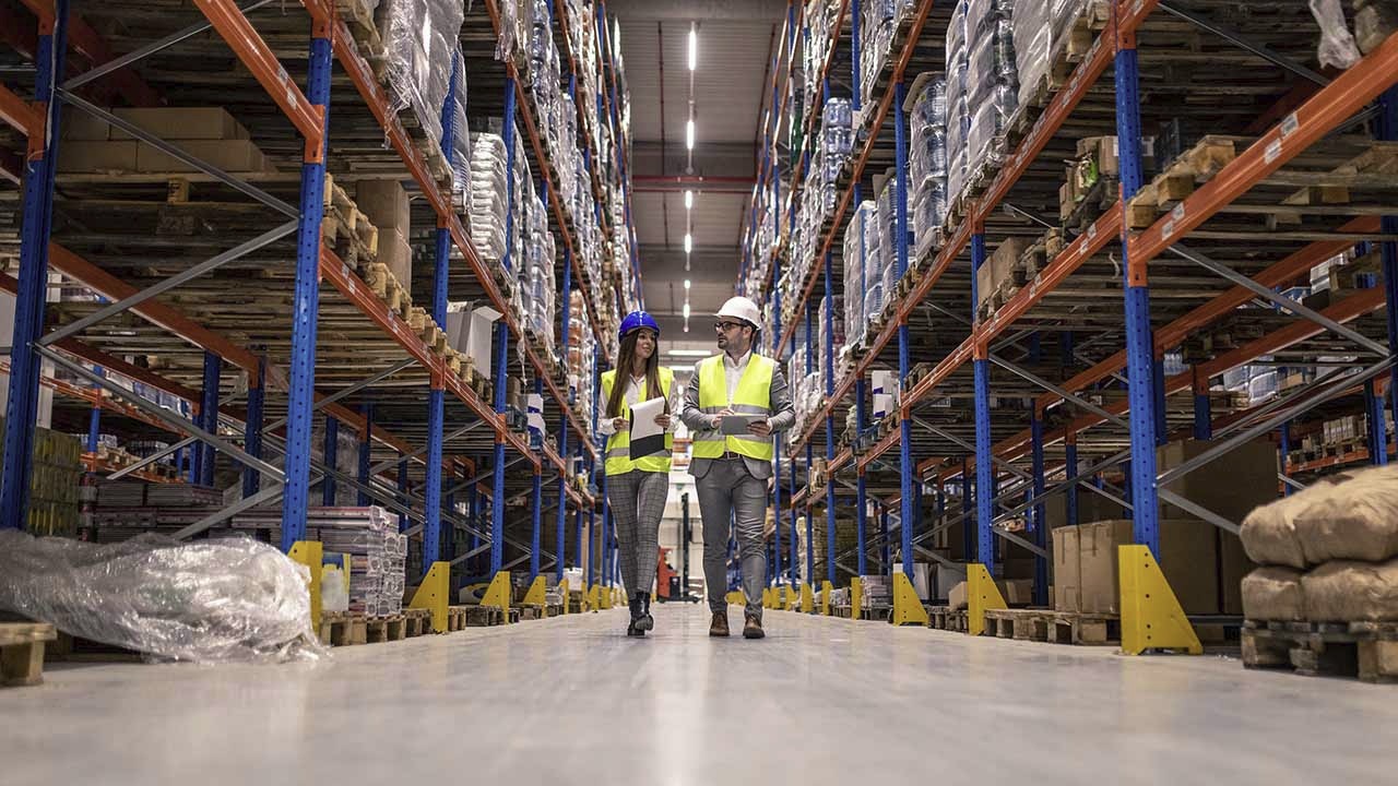 Auditors walking a warehouse aisle with checklists during a site audit